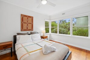 Ein Schlafzimmer mit Bett, Nachttisch, Fenster mit Blick auf Grünflächen und Deckenventilator.