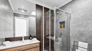 A modern bathroom with a glass shower enclosure, a wooden vanity, and a large mirror. - Surphy G (Anglesea)