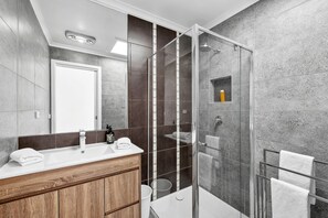 Ein modernes Badezimmer mit einer Duschkabine aus Glas, einem Holzboden und einem großen Spiegel.