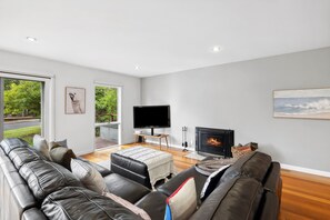 Un salon moderne avec un canapé en cuir, un t éléviseur à écran plat, une cheminée et une grande fenêtre donnant sur un paysage verdoyant.