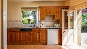 Una cocina con armarios de madera, lavavajillas, refrigerador y ventana con vista a zonas verdes.