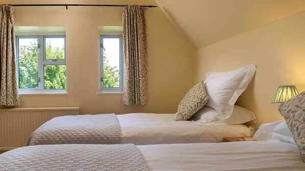 A bedroom with two beds, a window with curtains, a lamp, and a view of greenery outside. - Hilcot Farmhouse - pet-friendly rural farm retreat near Cheltenham (Near Cheltenham)