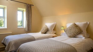 Habitación con dos camas, cada una con colcha acolchada y almohadas a juego. Se observa una ventana con cortinas, una lámpara de noche y un radiador.