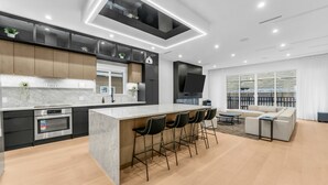 Una cocina moderna con una isla central, taburetes de bar, horno empotrado y un ventanal con vistas a un balcón.