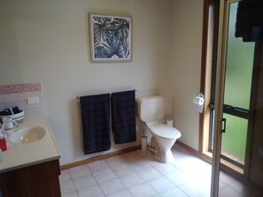 Une salle de bain équipée d’un lavabo, de deux serviettes, de toilettes et d’une fenêtre donnant sur un espace verdoyant.