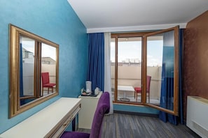 Une chambre d’hôtel avec un grand miroir, un bureau, une chaise violette, une petite table avec une tasse blanche et une vue sur un espace extérieur aménagé en salon, accessible par une porte vitrée.