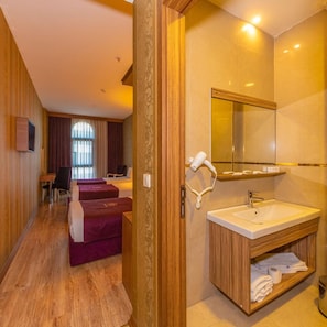 A hotel room with a wooden floor, a bed with a red headboard, a sitting area with a chair and a table, a bathroom with a sink and a mirror, and a window with curtains. - Interstellar Hotel (Istanbul)