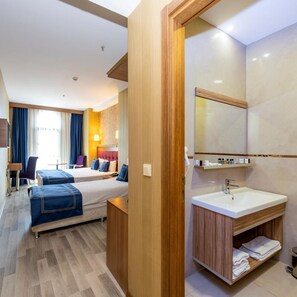 Habitación de hotel con cama, mesita de noche, espejo, lavamanos y ventana con cortinas.