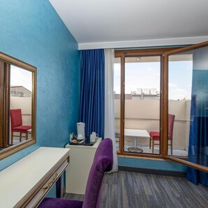 A hotel room with a desk, a purple chair, a coffee maker, and a view of the city through a large window. - Interstellar Hotel (Istanbul)