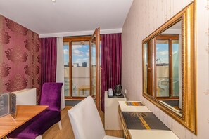 Habitación de hotel con escritorio de madera, una silla morada, sofá blanco y un espejo grande.