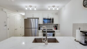A modern kitchen with white cabinetry, stainless steel appliances, a marble countertop, and under-cabinet lighting. - Cozy Place to Stay in South Calgary (Calgary)