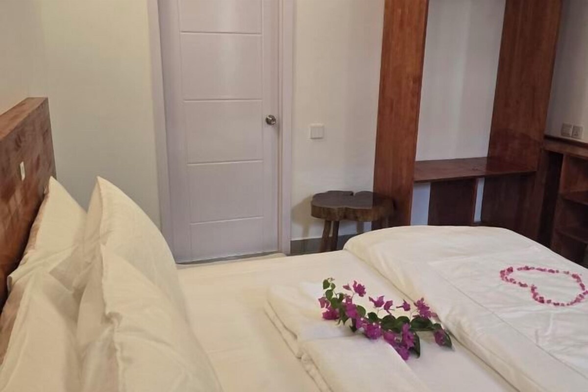 A neatly made bed with white linens and a heart-shaped decoration on the bedspread.