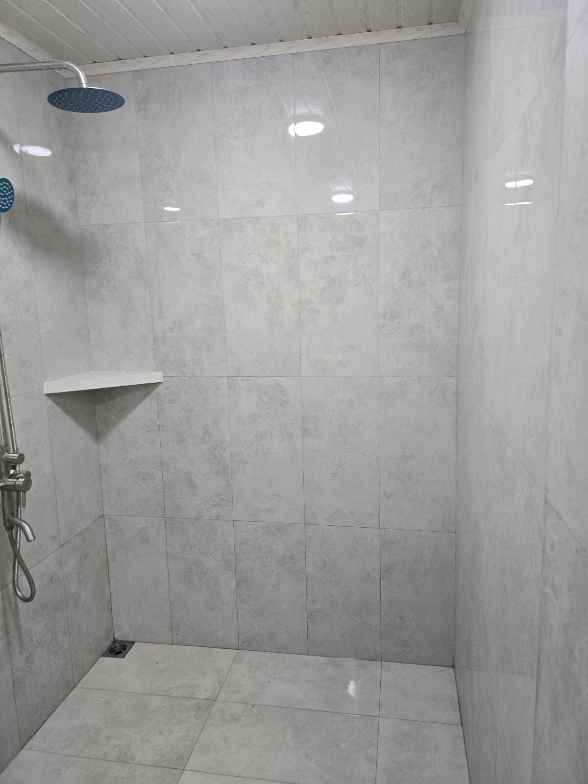 A small, tiled shower area with a handheld showerhead and a wall-mounted showerhead.