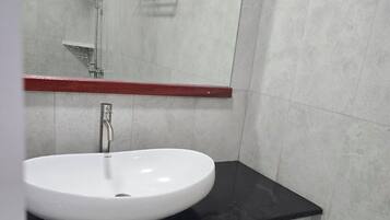 Un baño moderno con lavamanos blanco, encimera negra y paredes cubiertas de baldosas grises.