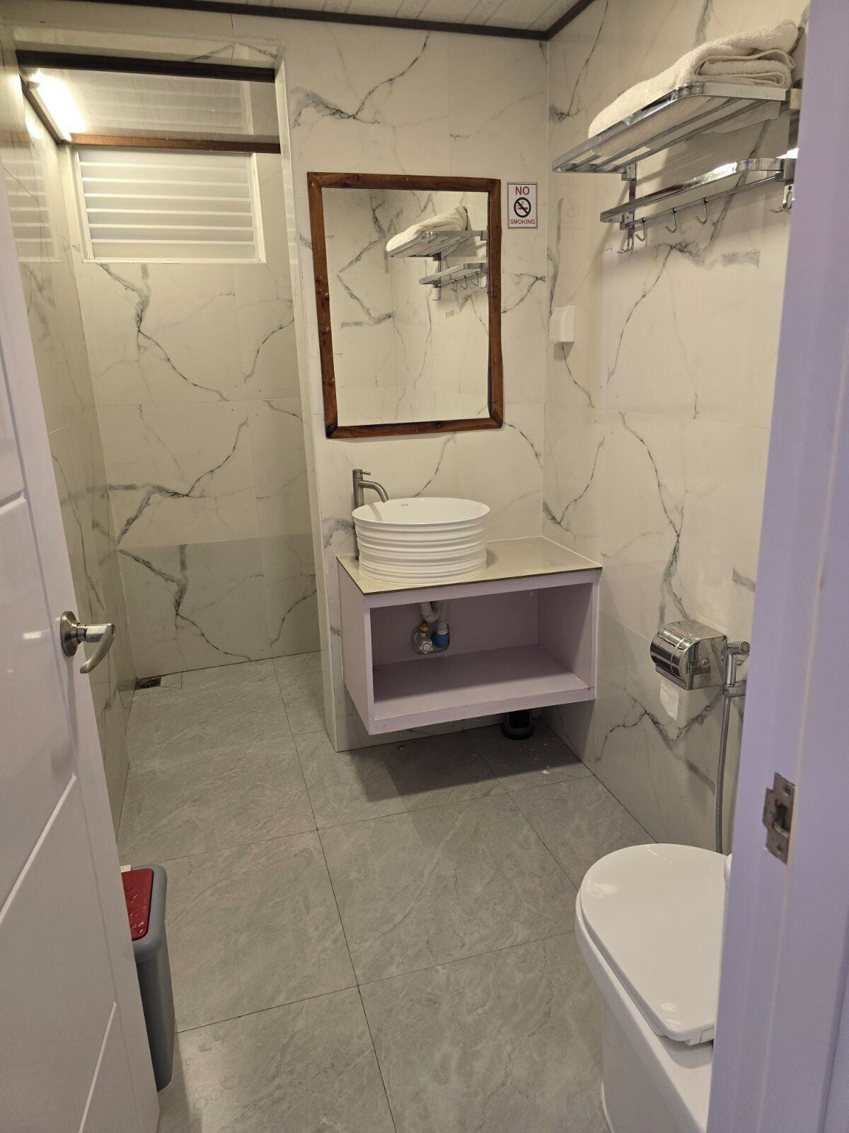 A bathroom with a marble wall, a sink with a mirror, a towel rack, and a shower.