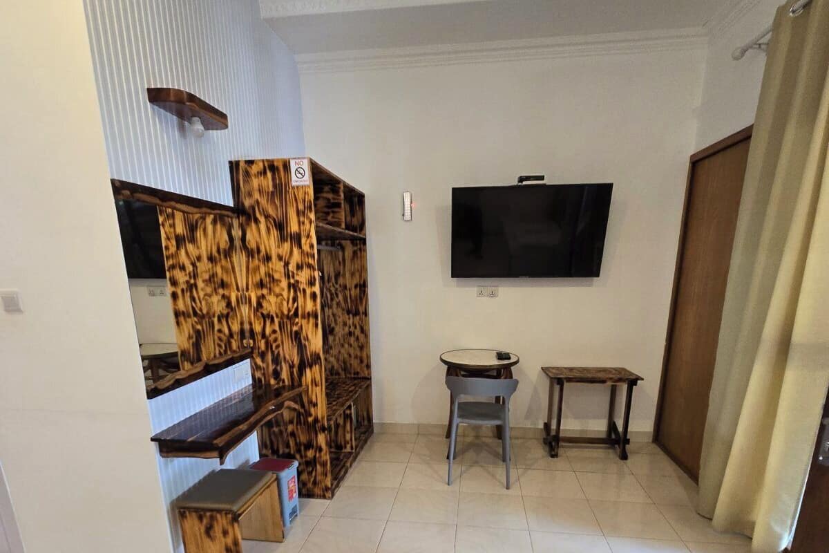 A spacious living room with a flat-screen TV mounted on the wall, a wooden bench, a small round table, and a sofa.