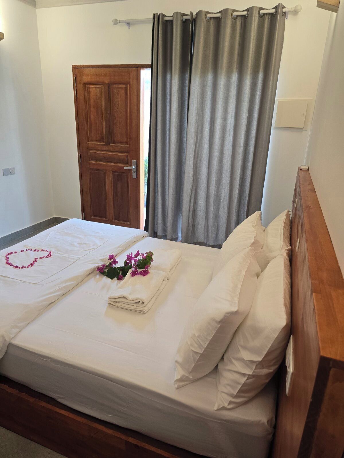 Una cama bien hecha con sábanas blancas, una decoración en forma de corazón y flores rosas.