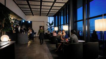 A modern lounge area with a bar, seating, and large windows offering a city view.