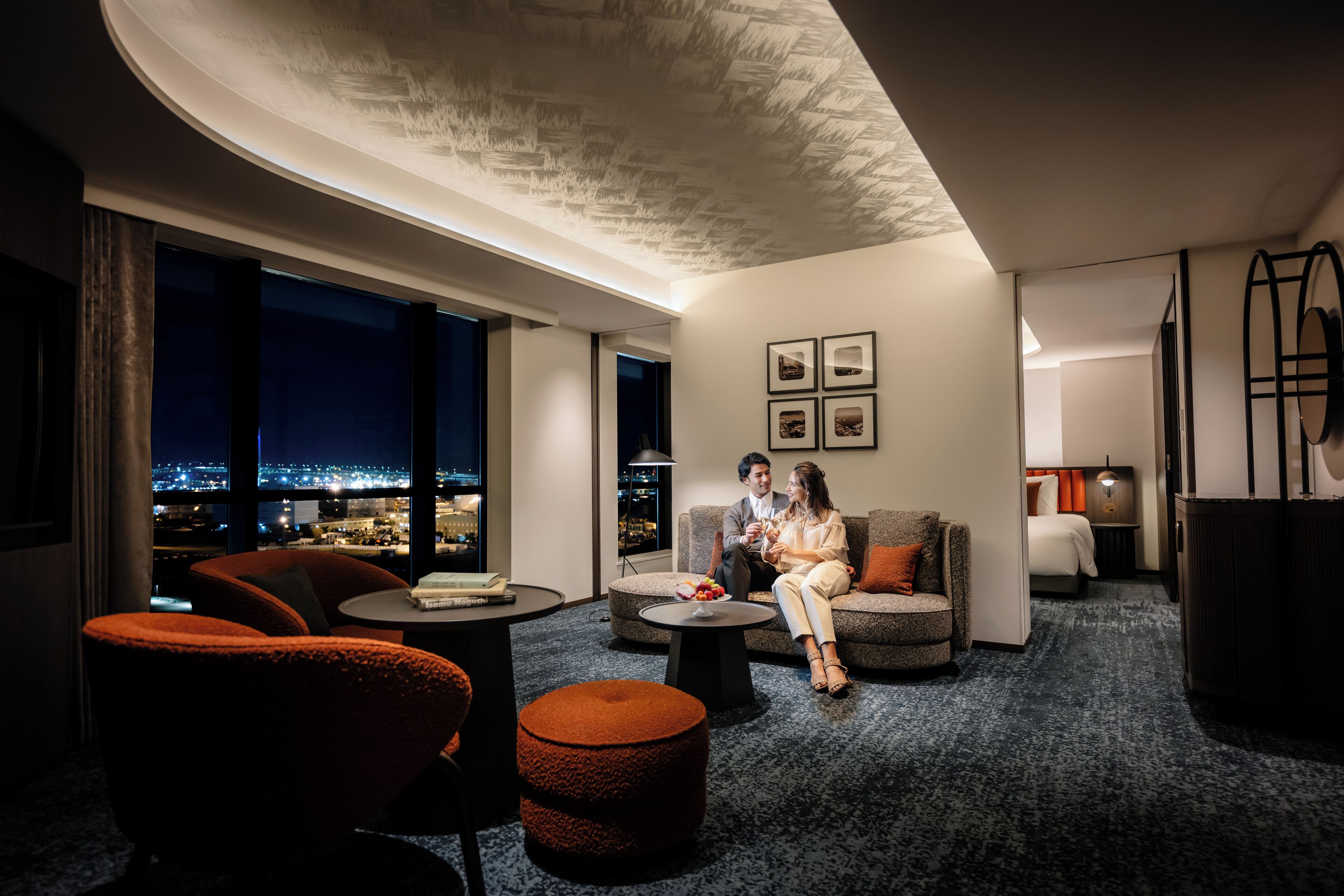 A modern hotel room with a city view, a cozy seating area, and a well-lit ambiance.