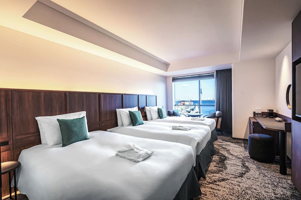 Une chambre d’hôtel avec trois lits, un bureau et une vue sur la ville.