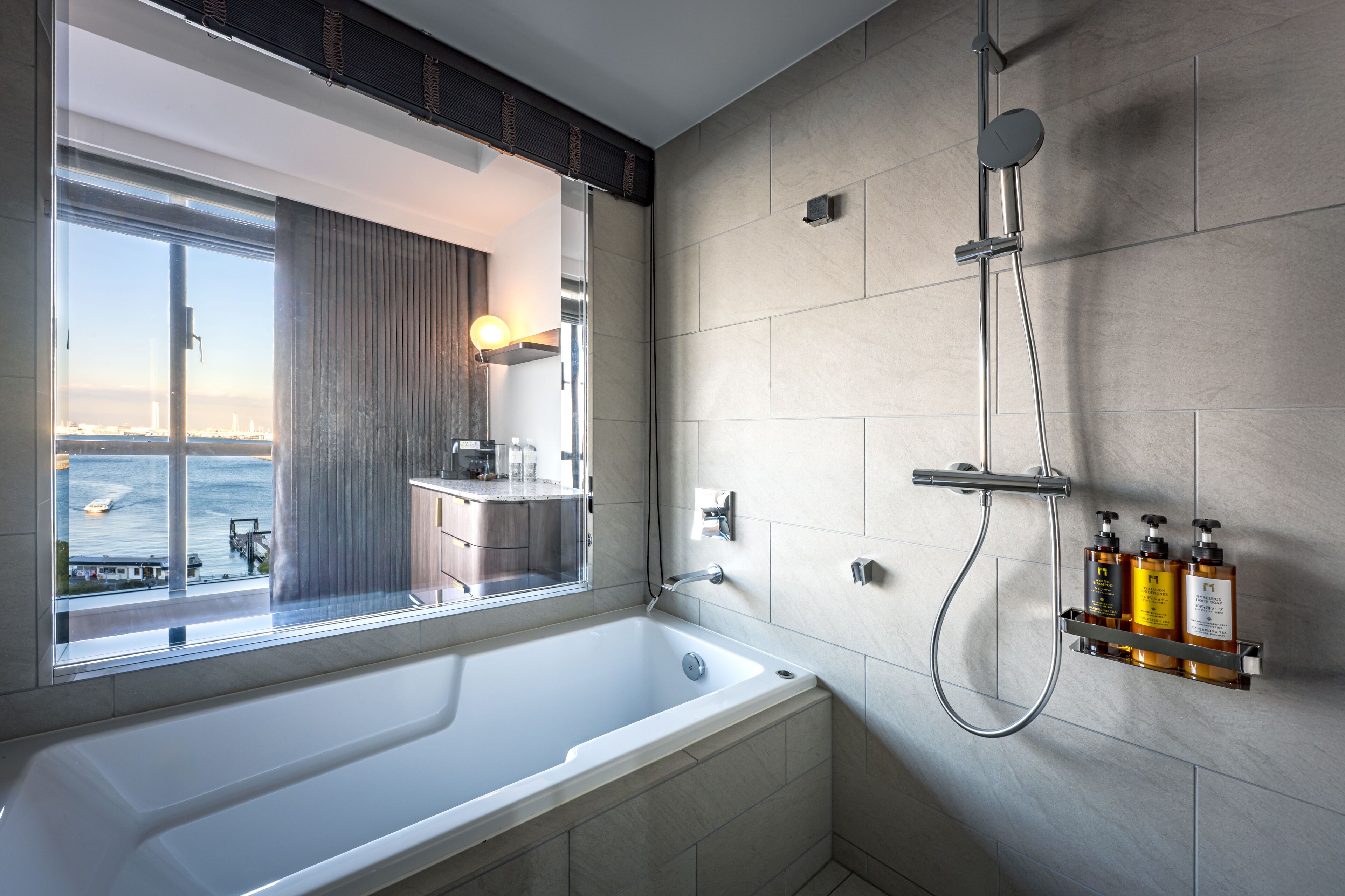 A modern bathroom with a large bathtub, a shower, and a window offering a view of the sea.