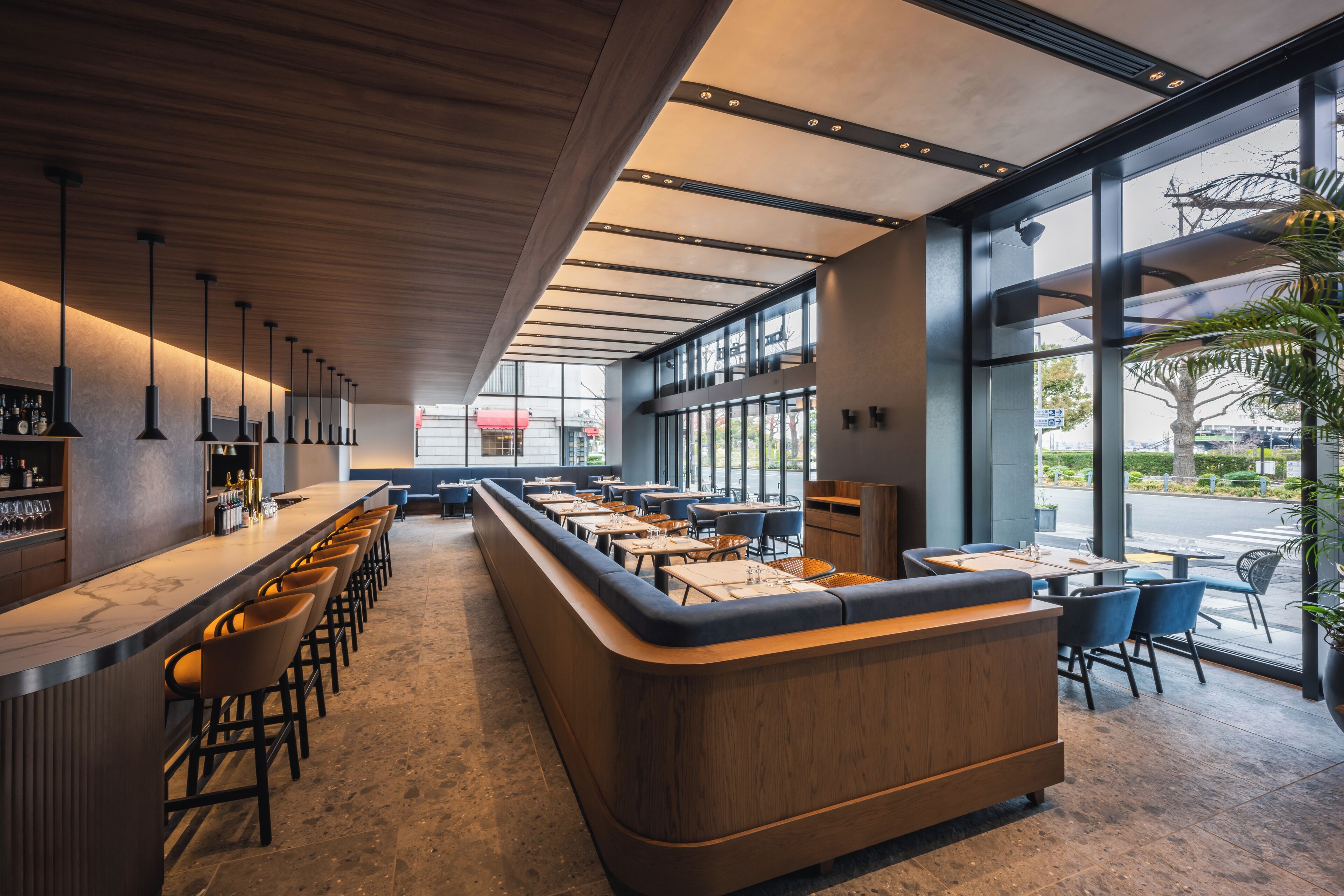 Eine moderne Bar mit einer langen Theke, Barhocker und einer Sitzgruppe mit Tischen und Stühlen.