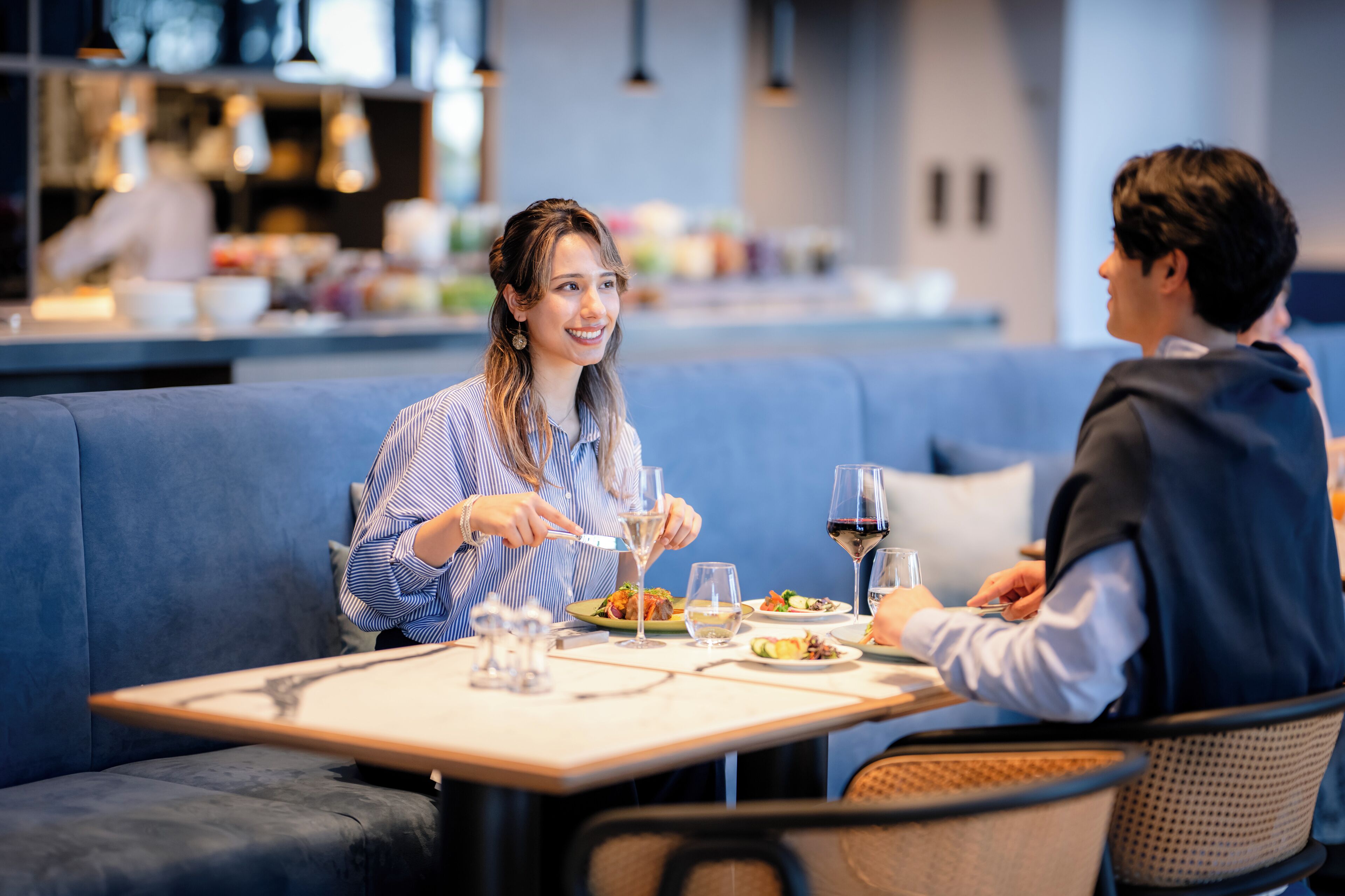 Un comedor con una mesa dispuesta para dos personas, un sofá azul y una cocina al fondo.