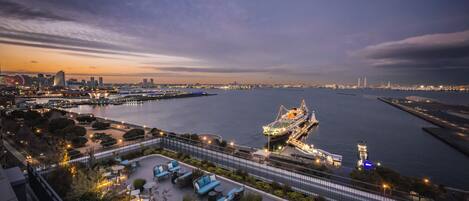Un hotel frente al agua con terraza al aire libre, vistas del horizonte de la ciudad y un gran barco amarrado cerca.