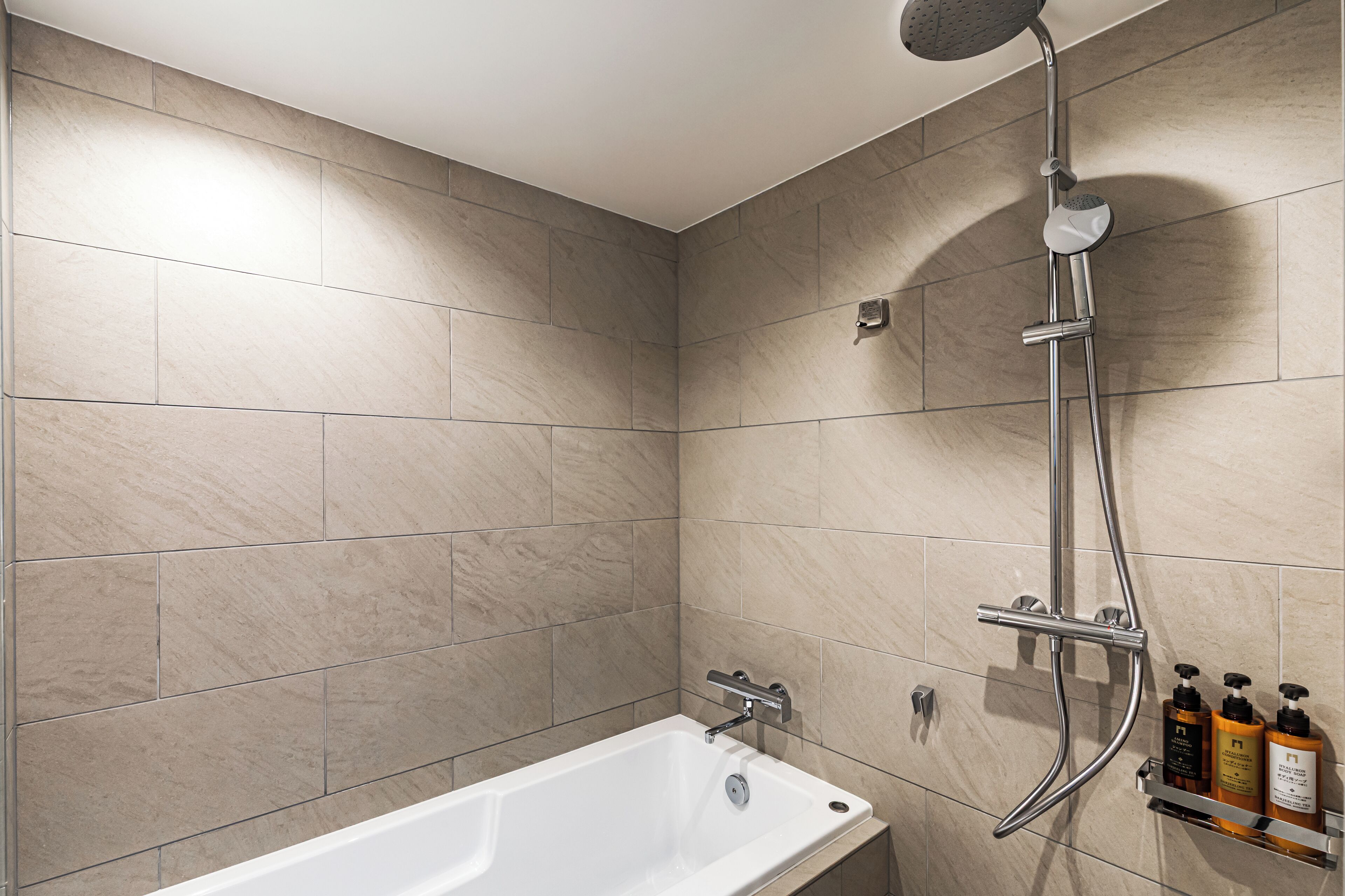 A modern bathroom with a bathtub, a showerhead, and a shelf with toiletries.