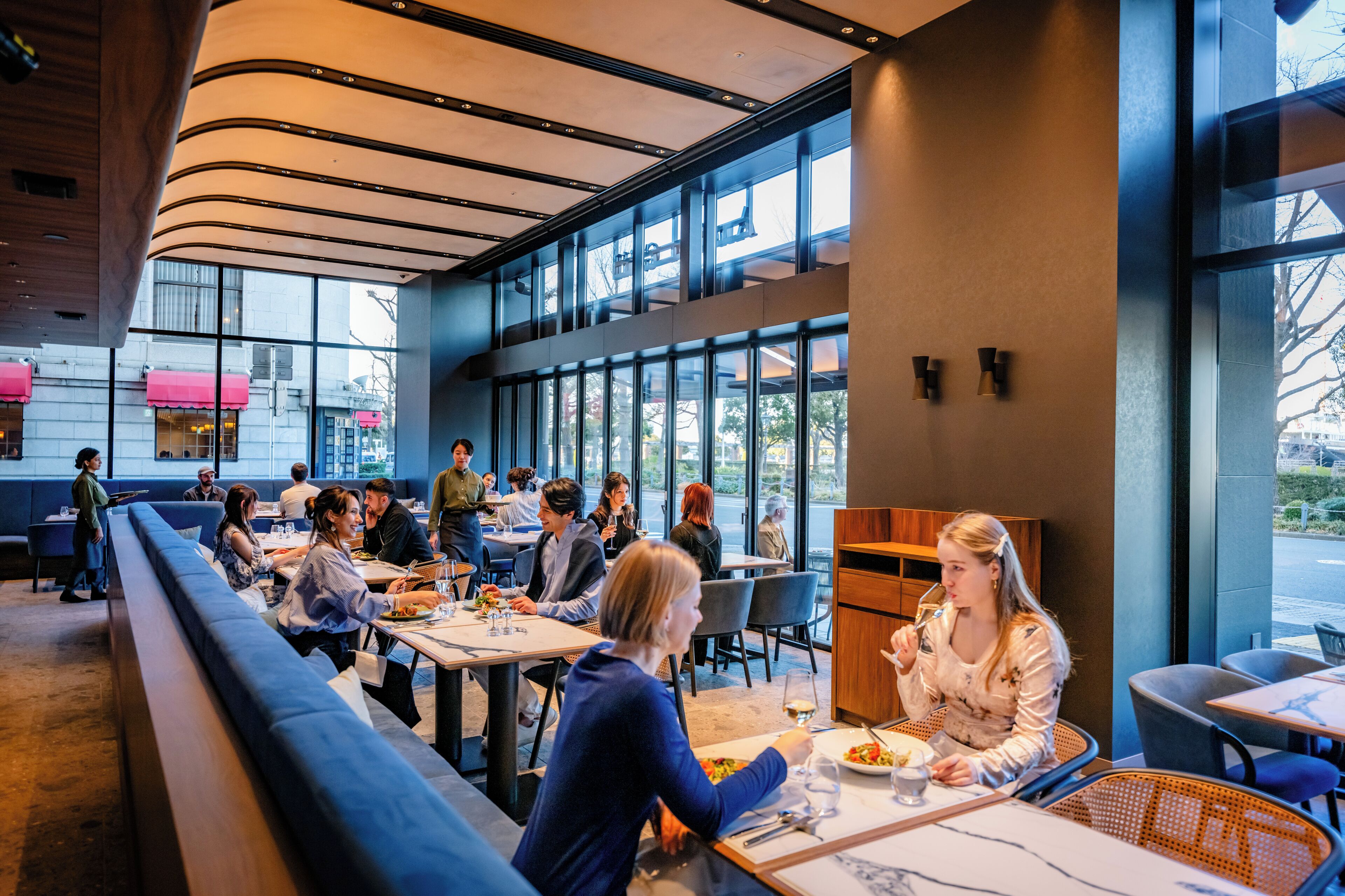 A modern restaurant with high ceilings, large windows, and a mix of seating including tables and booths.