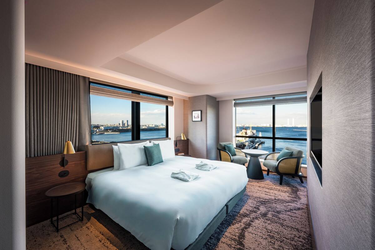 Une chambre d’hôtel moderne dotée d’un grand lit, d’un coin salon avec vue sur la ville et d’une grande fenêtre.