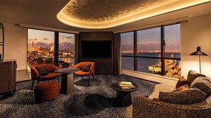 Ein modernes Wohnzimmer mit großem Fernseher, bequemen Sitzmöglichkeiten, Blick auf die Stadt und Stadtansicht durch große Fenster.