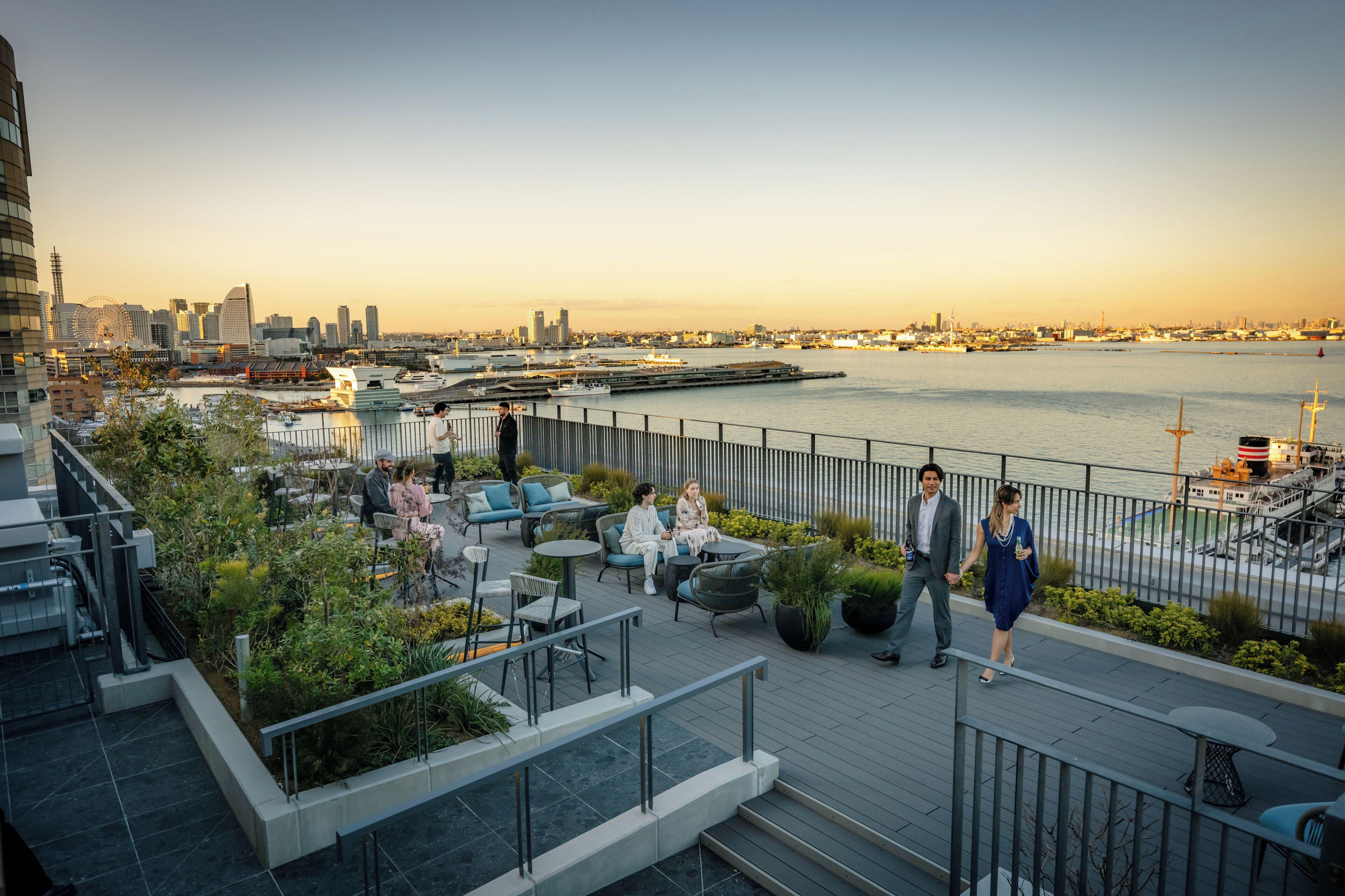 A rooftop terrace with outdoor seating, a view of the city skyline, and a waterfront.