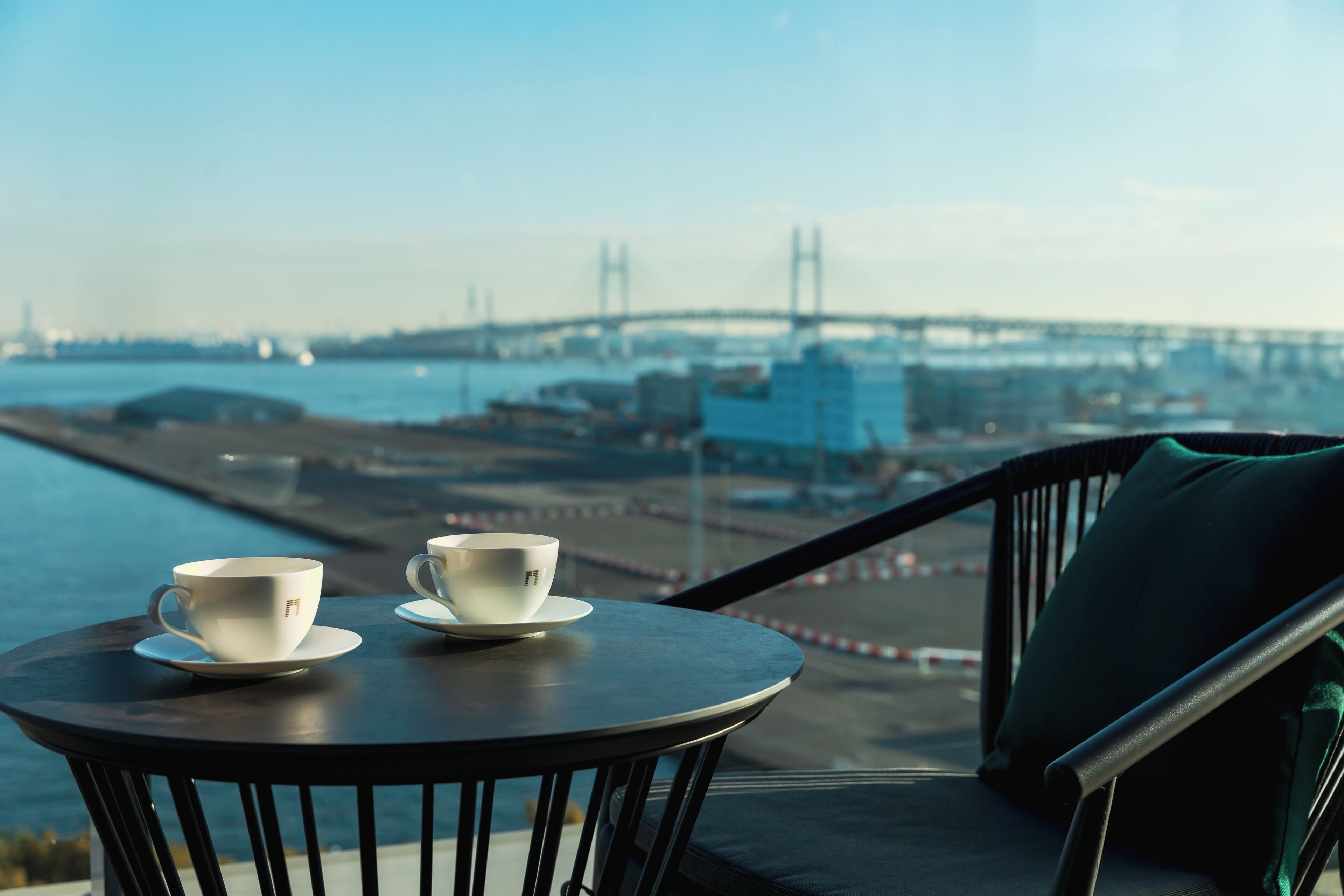 A balcony with two white cups on a saucer, overlooking a bridge and water.