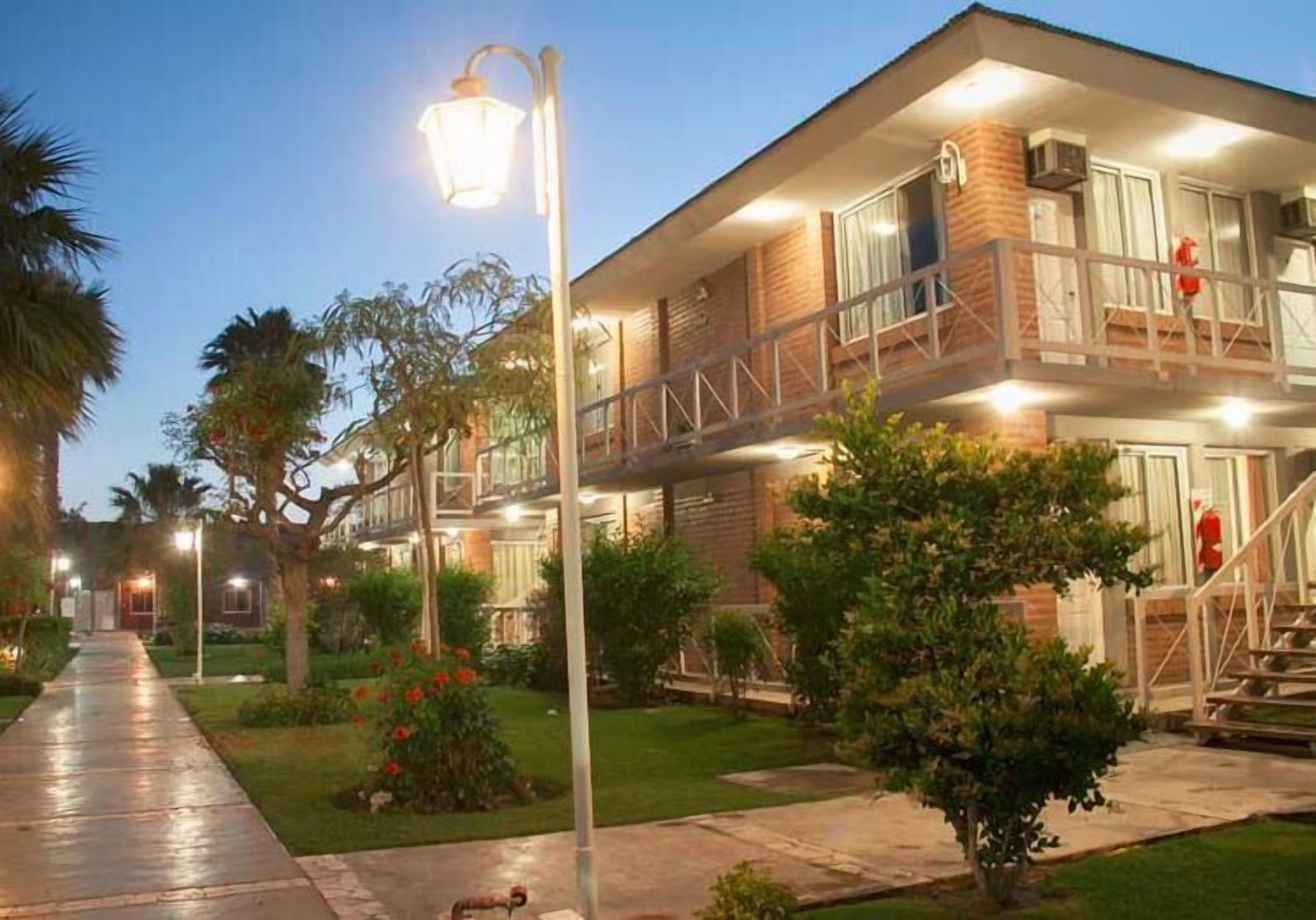 Un edificio de dos pisos con un balcón en el nivel superior, un corredor cubierto y una entrada bien iluminada.