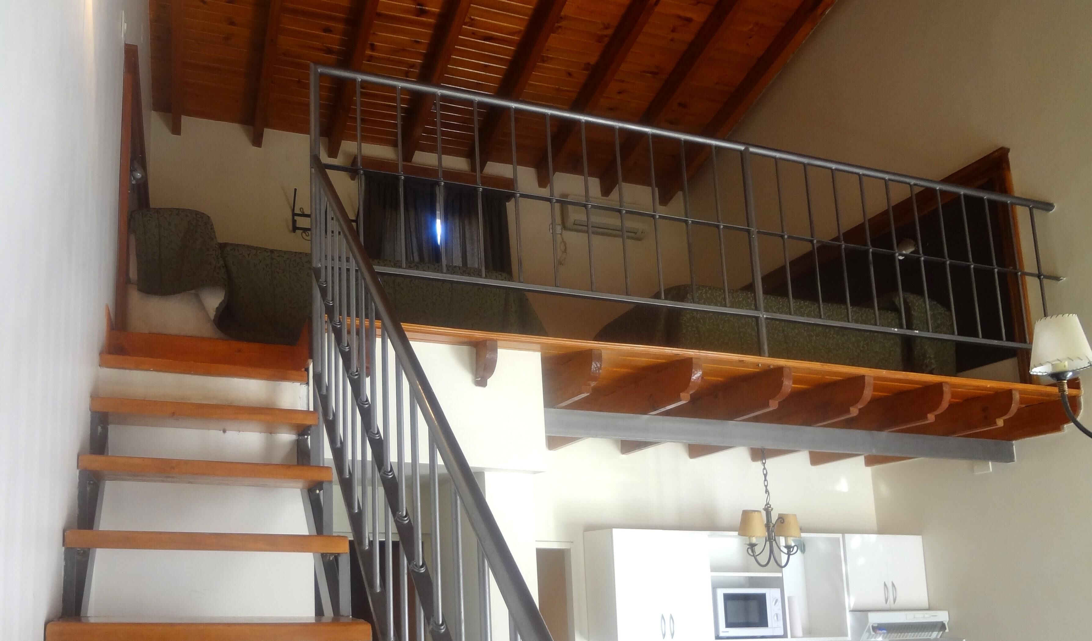 A staircase with wooden steps and metal railings, leading to a lofted area with a wooden ceiling and a chandelier.