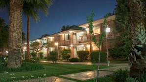 A multi-story hotel with a well-lit exterior, surrounded by lush greenery and palm trees.