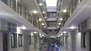 A modern hotel corridor with multiple floors, glass railings, and a central walkway with decorative lighting and plants.