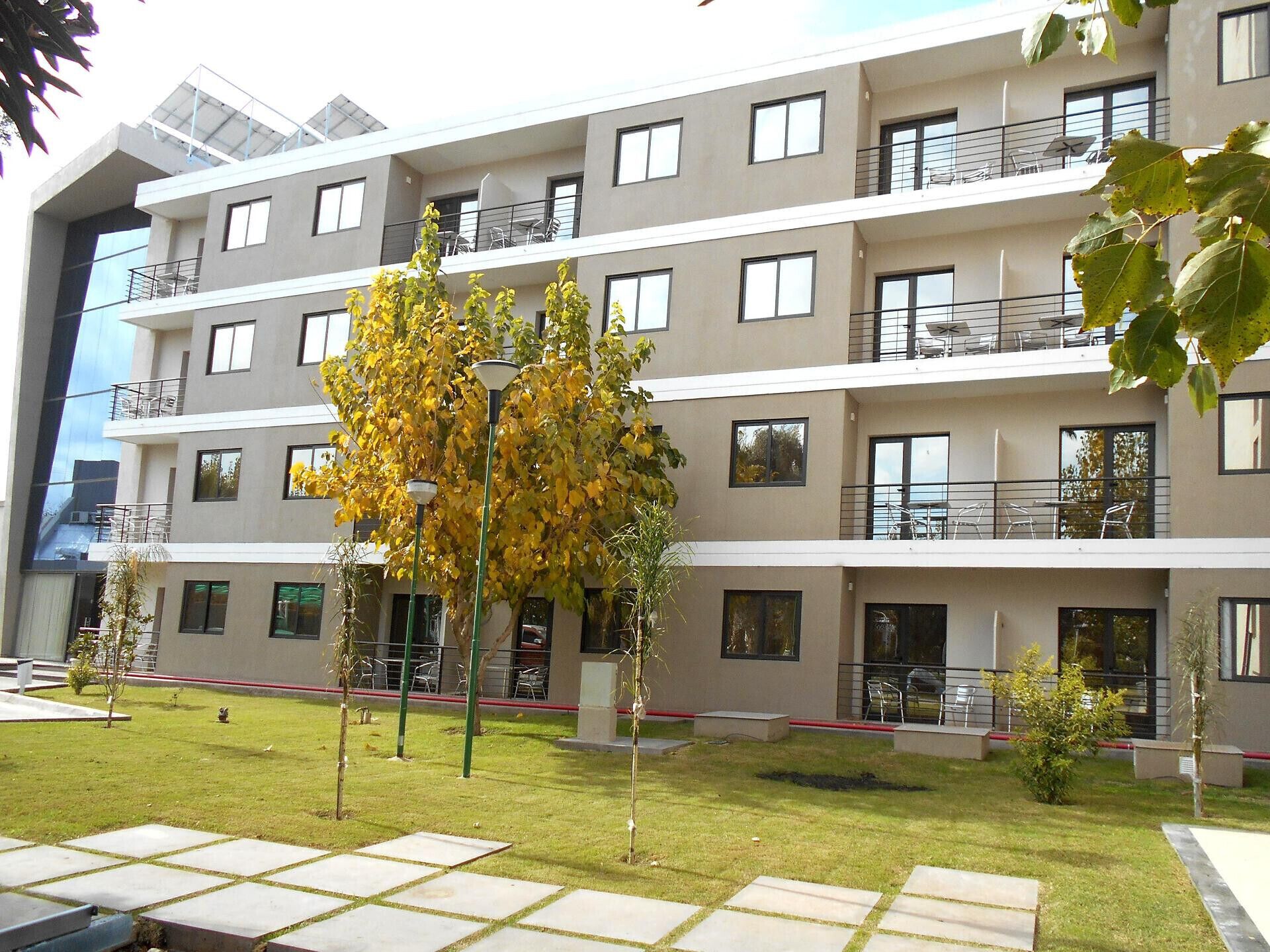 Un edificio a più piani con balconi, un cortile centrale alberato e un cielo sereno.