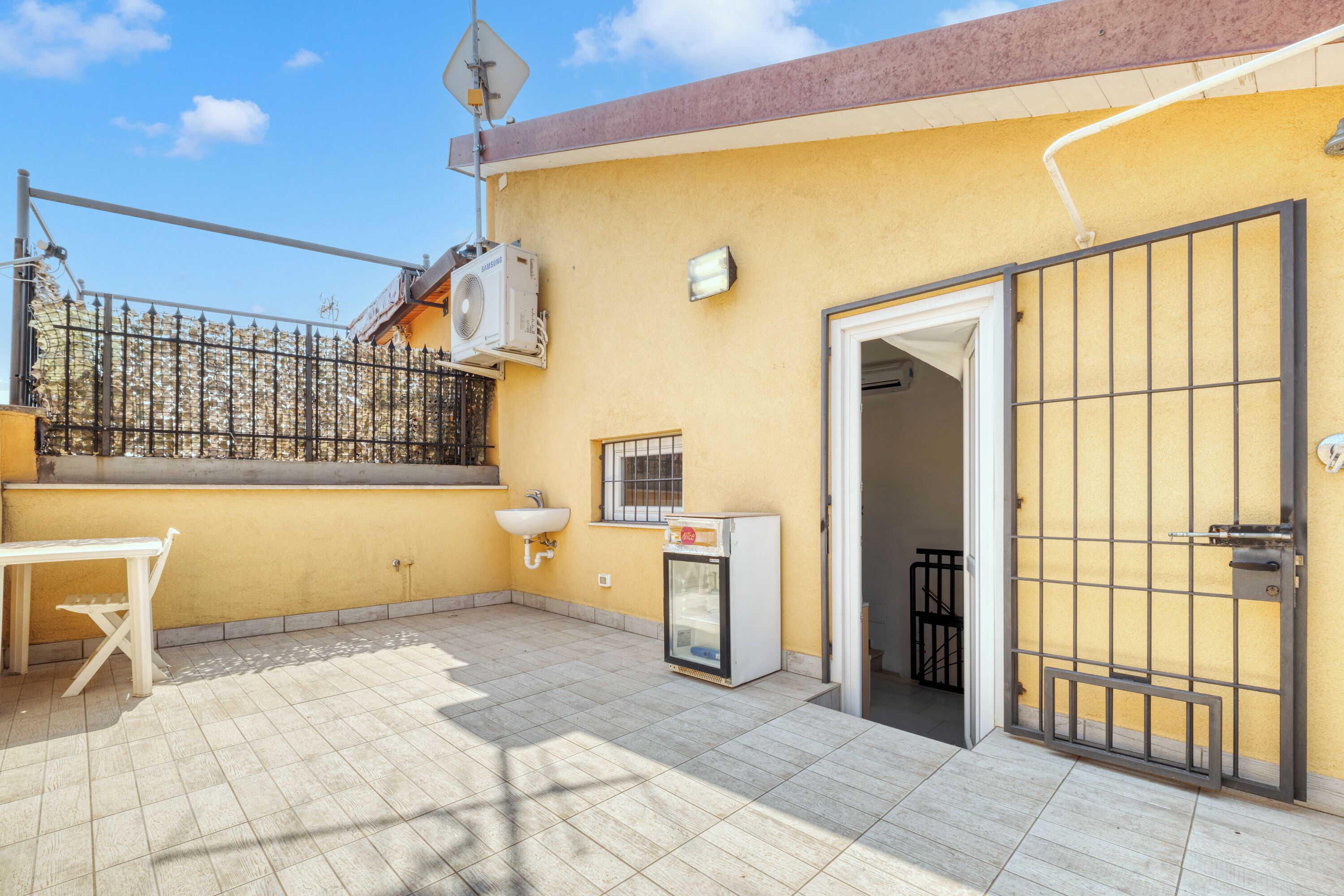A small outdoor patio with a table and chairs, a sink, and a refrigerator.