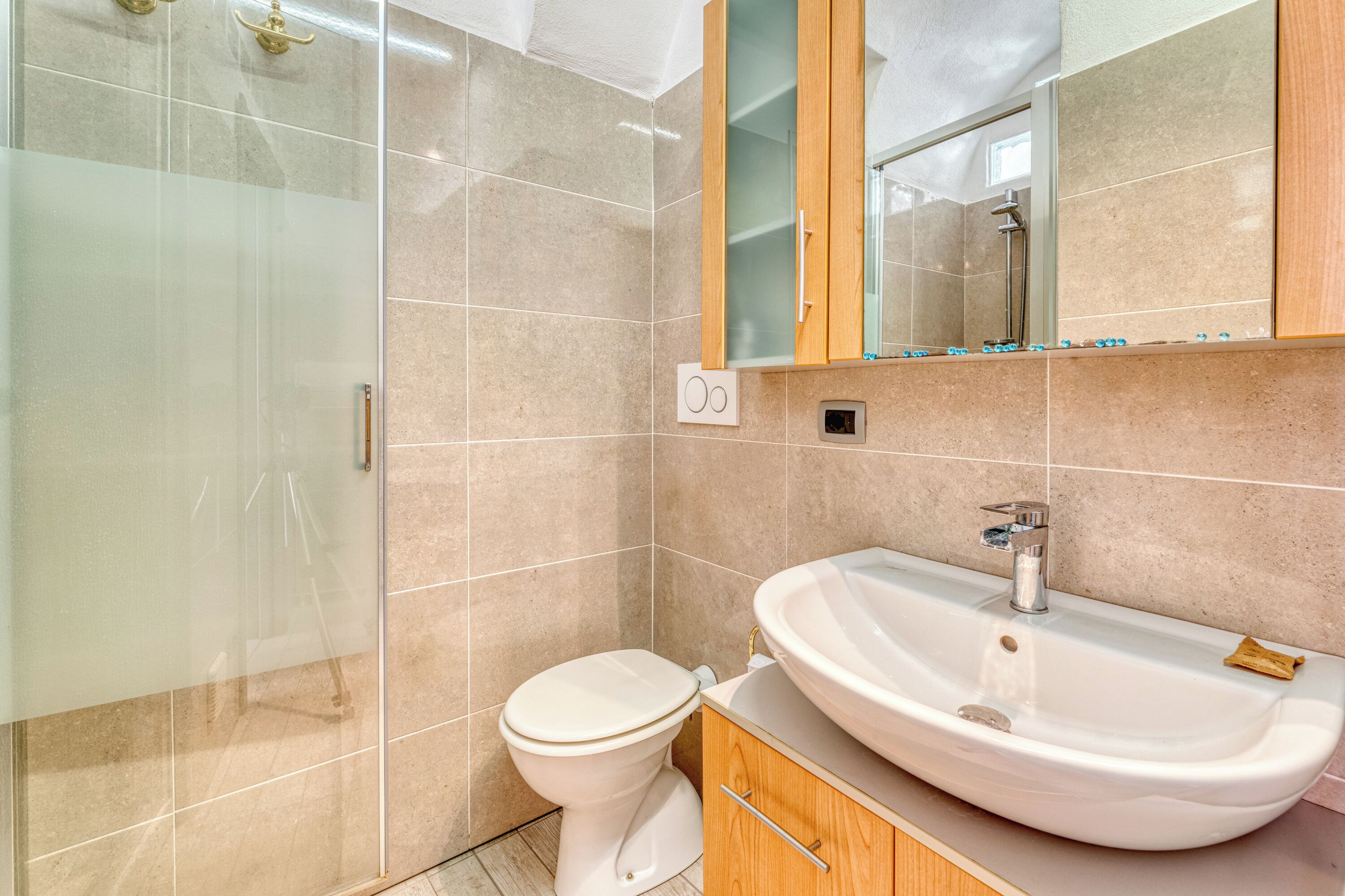 A bathroom with a glass shower enclosure, a white toilet, and a sink with a wooden cabinet.