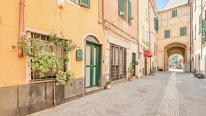 A narrow street with buildings featuring arched doorways and green shutters. - Sea Stone - 100m From The Sea (Borghetto Santo Spirito)