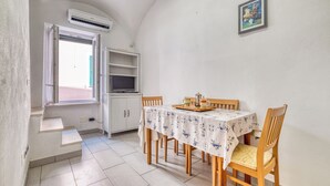 A dining area with a table set for two, a window with an open shutter, and a white air conditioning unit mounted on the wall. - Sea Stone - 100m From The Sea (Borghetto Santo Spirito)