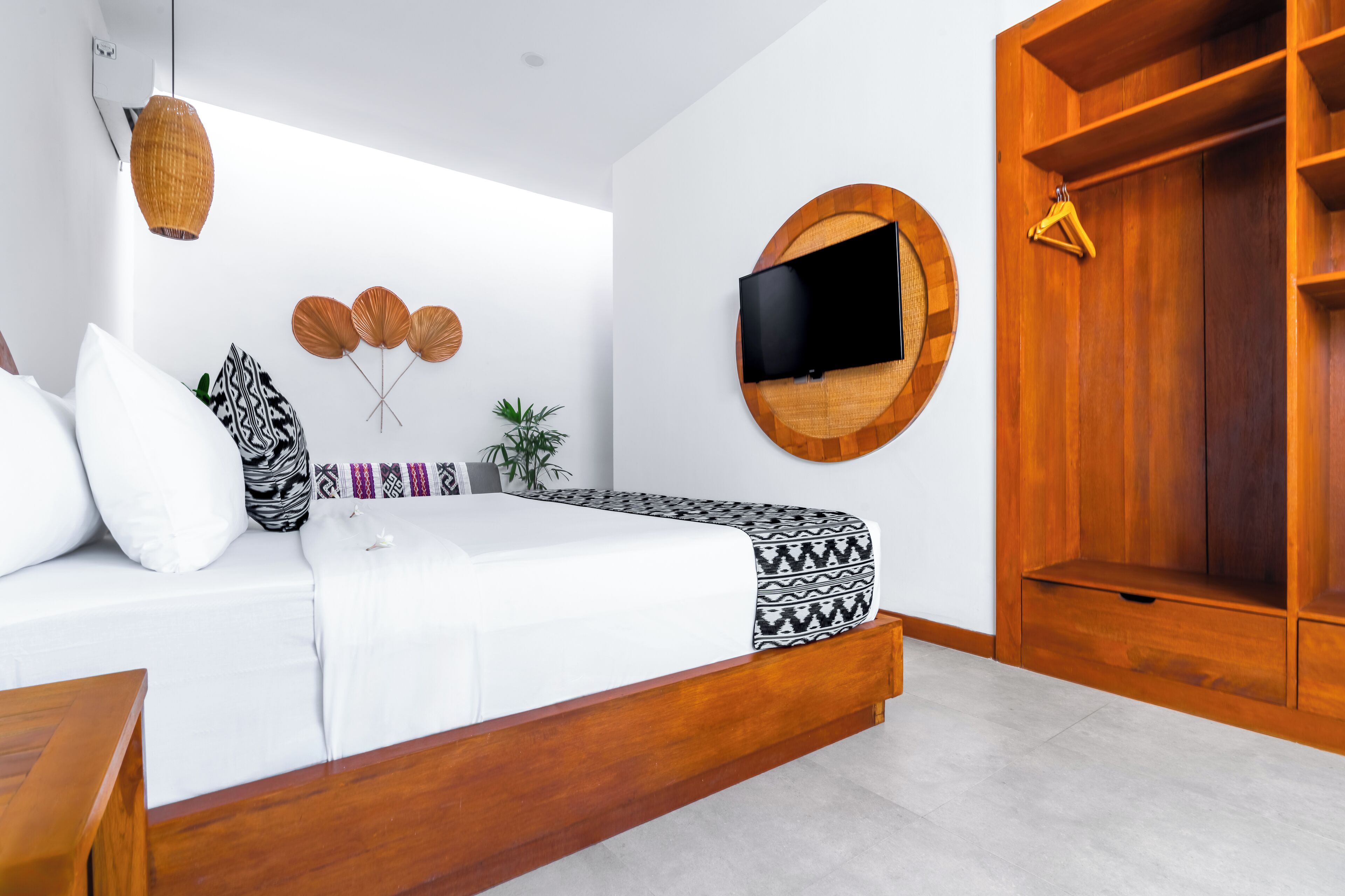 Une chambre à coucher moderne avec un lit, un téléviseur fixé au mur, une armoire en bois et un luminaire suspendu.