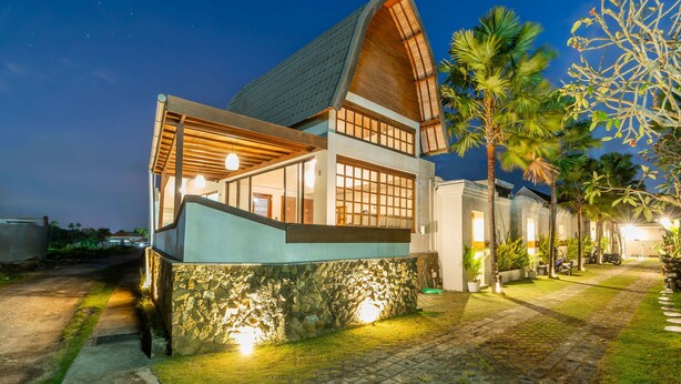Una moderna casa con tetto spiovente e ampie finestre, circondata da un giardino con palme e un vialetto lastricato.