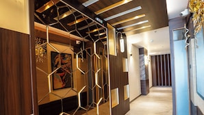 Un couloir moderne avec un lambris en bois, un luminaire aux formes géométriques et un sol en marbre.