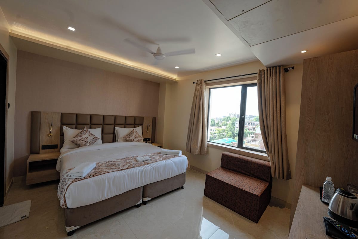 Une chambre d’hôtel moderne avec un grand lit, un petit canapé, une fenêtre avec des rideaux et un téléviseur à écran plat.