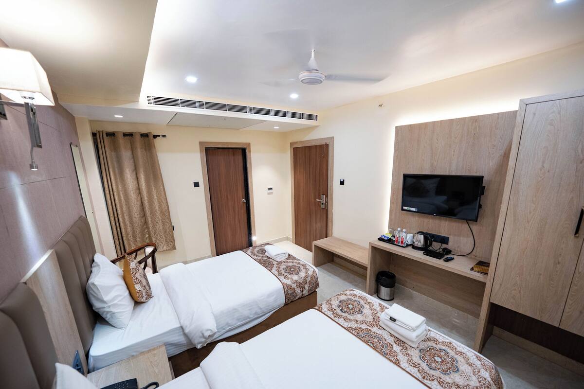 Une chambre d’hôtel avec deux lits, une télévision, un bureau avec une machine à café et un ventilateur de plafond.