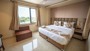 Une chambre d’hôtel avec un grand lit, un coin salon, un ventilateur de plafond et une fenêtre avec des rideaux.