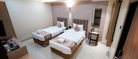 A hotel room with two beds, a desk with a chair, a small table, and a bathroom with a mirror and towel rack.